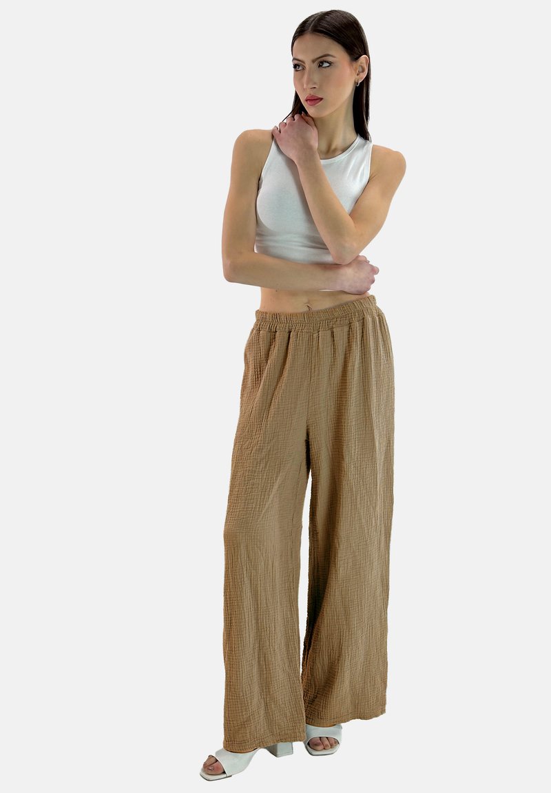 Lichtbruine, gestructureerde wijde broek met een elastische taille, gecombineerd met een strakke witte mouwloze top en lichtgekleurde haksandalen.