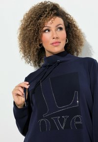 Mörkblå sweatshirt med hög krage, dragsko och en stor framsida med grafiken "love" accentuerad av rhinestones.