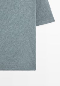 T-shirt en coton gris chiné à manches courtes avec texture de tissu visible et ourlet simple cousu sur fond blanc.