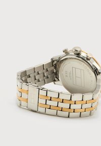 Ρολόι χειρός Tommy Hilfiger με μπρασελέ από ασημί και χρυσούς μεταλλικούς κρίκους και πίσω μέρος από ανοξείδωτο ατσάλι που εμφανίζει το λογότυπο και τις λεπτομέρειες αντοχής στο νερό.