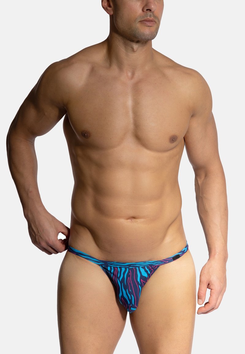 Blaue und lila gemusterte Schwimmbrieftaschen mit niedrigem Schnitt, deutlich erkennbaren wellenförmigen Linien und dünnen Trägern. Hergestellt aus glattem, dehnbarem Stoff.