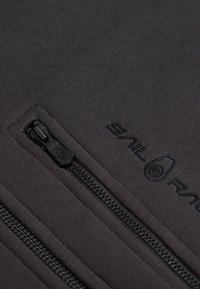 Schwarzer Fleece-Stoff mit zwei Reißverschlusstaschen, geprägtem Logo und strukturiertem Nähen für Langlebigkeit. Die Reißverschlusszüge sind elegant und funktional.