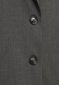 Cappotto in tessuto grigio con una texture liscia, design a un petto e due bottoni neri con quattro fori ciascuno.