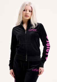 Fekete velúr melegítő szett cipzáras dzsekivel és nadrággal. A mellkason és az ujjon rózsaszín "Angel" és "Juicy" logók találhatók. Simább textúra, testhezálló szabás.