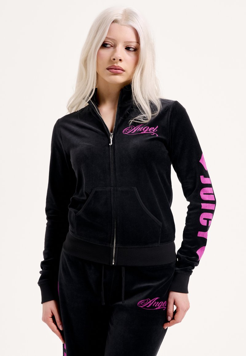 Fekete velúr melegítő szett cipzáras dzsekivel és nadrággal. A mellkason és az ujjon rózsaszín "Angel" és "Juicy" logók találhatók. Simább textúra, testhezálló szabás.