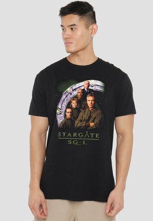 Black cotton t-shirt featuring a graphic of five characters from "Stargate SG-1" with a space-themed background in green and gray.
