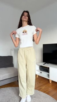 White short-sleeve t-shirt with a colorful graphic, paired with loose beige pants. Model is standing, revealing a casual outfit and white sneakers.
