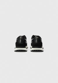 Baskets de sport noires avec un dessus en cuir lisse et des accents en daim. Elles comportent une semelle intermédiaire blanche et une semelle extérieure en caoutchouc noir texturé.