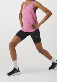 Růžový bezrámový sportovní top, černé cyklistické šortky a černé sportovní boty s bílými ponožkami. Výrazné logo na topu a šortkách.