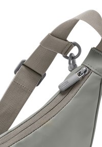 Borsa a tracolla grigia caratterizzata da un materiale liscio, una tracolla testurizzata in contrasto, una zip grigia e una forma curva e triangolare.