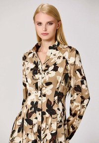 Robe chemise florale beige, dotée d'un devant à boutons, de manches longues et d'un motif ornée de fleurs blanches et noires.