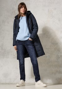 Navy puffer coat with a hood, light blue knit sweater, dark denim jeans, and white sneakers. Smooth texture, functional zippers, and casual fit.