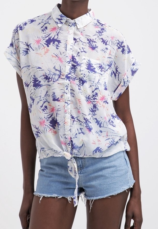 Biała koszula z kwiatowym wzorem w fioletowe i różowe motywy. Krótkie rękawy i przewiązana w talii. W połączeniu z postrzępionymi szortami dżinsowymi.