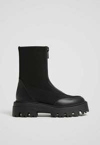 Bottines noires avec une tige en tissu lisse et extensible, une fermeture éclair latérale et une semelle en caoutchouc épaisse et texturée pour une meilleure adhérence.