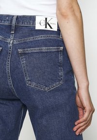 Mörkblå denimjeans med en subtil textur. Bakifrån syns två traditionella fickor och en vit Calvin Klein-label i midjan.