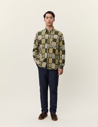 Koszula zapinana na guziki w żółto-zielono-beżową kratę; długie rękawy; kieszeń na piersi; zestawiona z granatowymi spodniami; brązowe buty.