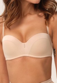 Beżowy satynowy biustonosz z formowanymi miseczkami, wsparciem w postaci fiszbin, regulowanymi ramiączkami oraz małym detalem z cyrkonią na środku jako akcent.