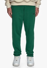 Grønne sweatpants med en afslappet pasform, der har en broderet logo-detail. Parret med hvide sportssko, som viser en afslappet stil.