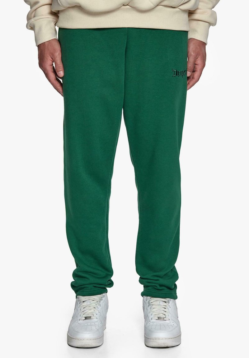 Grønne sweatpants med en afslappet pasform, der har en broderet logo-detail. Parret med hvide sportssko, som viser en afslappet stil.
