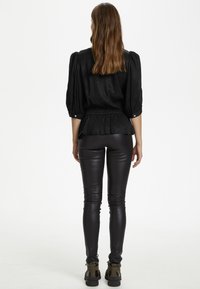 Blusa negra con mangas abullonadas y cintura elástica, combinada con legging de cuero sintético negro y botas de tacón grueso.