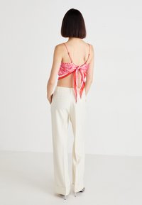 Ružičasti uzorčasti crop top s vezanjem straga, uparen s kremasto-bijelim hlačama visokog struka. Glatka tkanina s tankim naramenicama i slobodnim krojem.