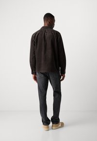 Brown corduroy shirt with vertical stripes, button-down collar, and cuffed sleeves, paired with dark jeans and beige shoes.