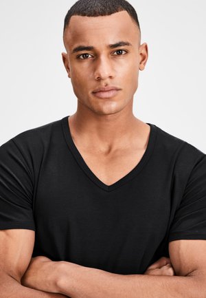 Schwarz V-Ausschnitt T-Shirt aus glattem Stoff, enganliegendes Design, kurze Ärmel, mit einer Nahaufnahme des Oberkörpers eines Modells und gekreuzten Armen.