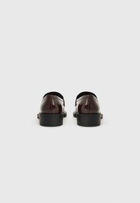 Chaussures en cuir verni bordeaux avec un bout arrondi, un talon noir et une texture lisse, arborant un design minimaliste et un style sans lacets.