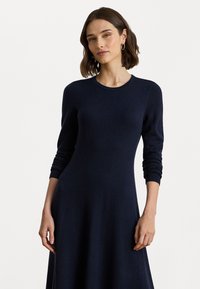 Marineblå strikkekjole med lange ermer, rund hals og en tettsittende liv som glir ut i et løst skjørt. Myk tekstur og glatt finish.