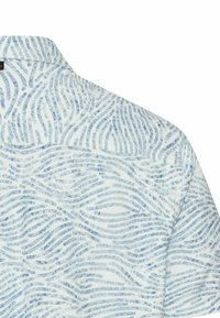 Witte stof met lichtblauwe, abstracte golfpatronen die op vingerafdrukken lijken, op het bovenste rug- en schoudergedeelte van een shirt.