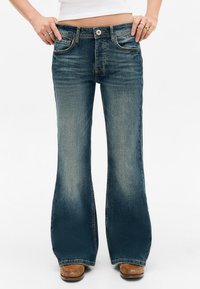 Vervaagde blauwe denim flared jeans met vijf zakken, een knoopsluiting en contrasterende stiksels. Gladde textuur met een lichte glans.