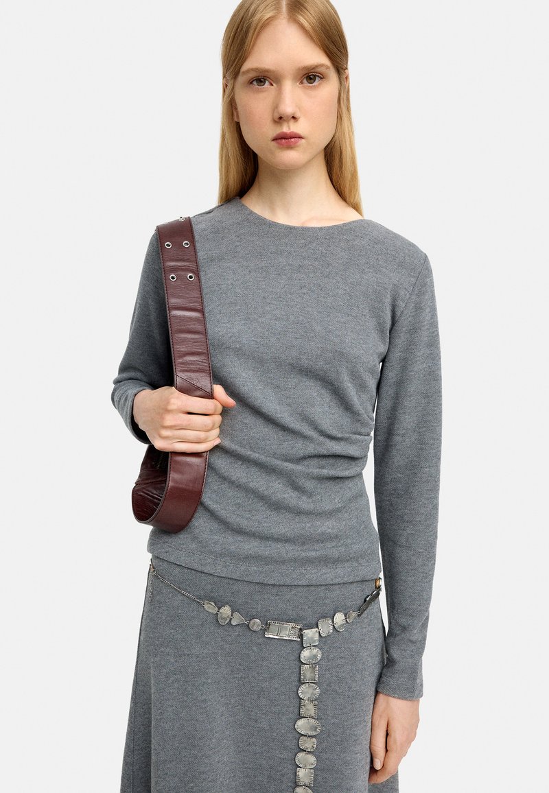 Szary sweter z długim rękawem z okrągłym dekoltem, w zestawieniu z ciemnobrązową skórzaną torbą na ramię i metalową dekoracyjną paskiem w srebrnym odcieniu.