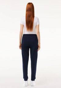 Marinen joggebukser med elastisk midje, tapered mansjetter og sidelommer, kombinert med en hvit tettsittende t-skjorte. Glatt stoffetekstur.