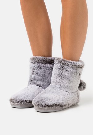 Chaussons gris en fourrure avec une texture douce, de hauteur courte, à bout rond et avec un revers moelleux, arborant un petit pom-pom sur l'arrière.