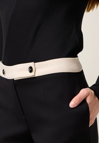 Zwarte kledingstuk met een gladde textuur, voorzien van een contrasterende beige riem met twee zwarte knopen en een slanke, op maat gemaakte fit.