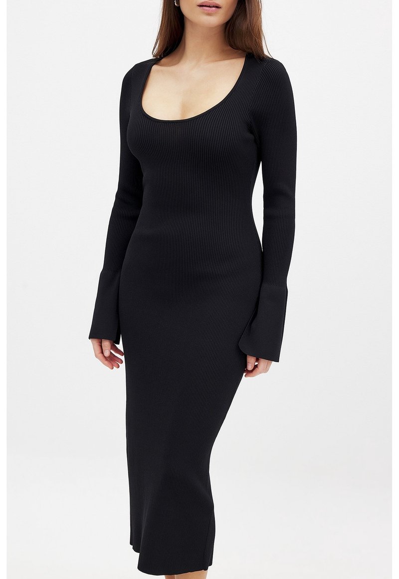 Robe noire côtelée avec un décolleté rond, manches longues et poignets évasés. Longueur mi-mollet, texture douce, coupe ajustée.