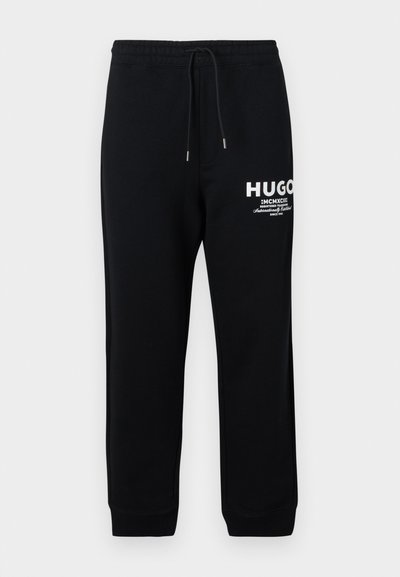 Pantalons de survêtement noirs en mélange de coton, avec une taille à cordon, des jambes fuselées et un logo et du texte imprimés blancs sur la cuisse gauche.