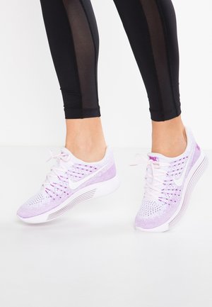 Stopy w białych i lawendowych butach do biegania Nike w połączeniu z czarnymi legginsami z przezroczystymi bocznymi panelami.