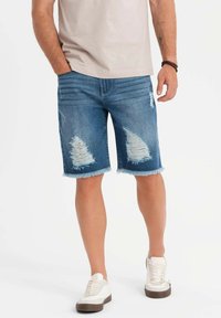 Jeansshorts i medelblått med slitna detaljer och fransade nederkanter, tillsammans med vita skor. Slät tyglig yta, avslappnad design.