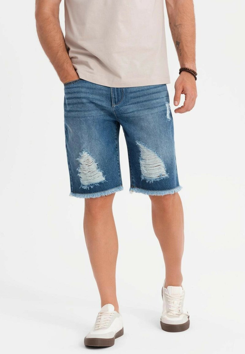 Jeansshorts i medelblått med slitna detaljer och fransade nederkanter, tillsammans med vita skor. Slät tyglig yta, avslappnad design.