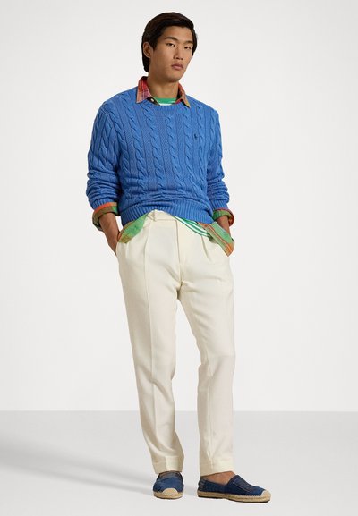 Blue cable-knit sweater over a multicolored collared shirt, cream trousers, and navy espadrilles with beige soles. Simple, casual design.