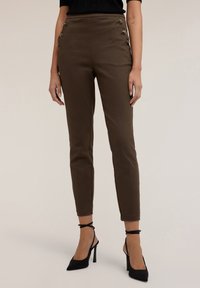 Pantaloni marroni a gamba affusolata con accenti di bottoni laterali, caratterizzati da una texture liscia e una vestibilità slim. Abbinati a scarpe nere con tacco alto.