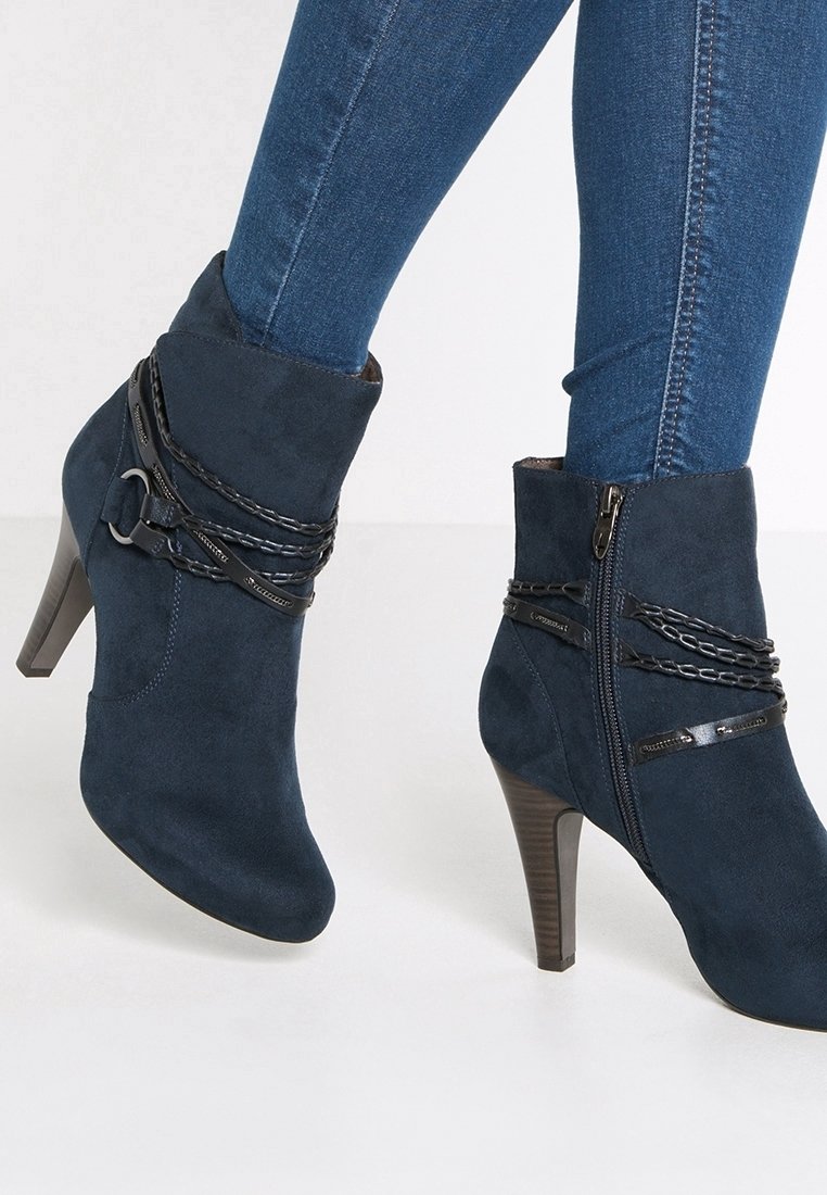 Botas de tobillo de ante azul marino con un tacón alto, con detalles de cadena negra y un cierre de cremallera lateral, diseño texturizado y elegante.