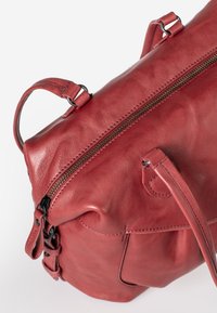 Red leather handbag with a textured finish, featuring a top zipper, adjustable strap, and side pocket with hardware accents.