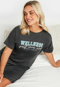 Abito t-shirt in cotone grigio con la scritta "WELLNESS self care club EST. 1987" in teal e bianco, maniche corte e vestibilità comoda.