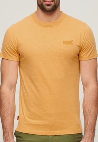 Kortærmet t-shirt med rund hals i sennepsgul, lavet af blød bomuld. Har subtil branding på brystet og en tekstureret, let finish.