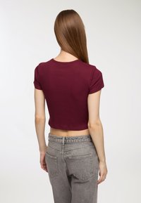T-shirt corto bordeaux con maniche corte e scollatura rotonda, abbinato a jeans grigi a vita alta con tasche posteriori e cintura elastica.