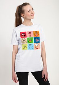 Hvid bomuld t-shirt med et gitter af tegneserieansigter i levende farver. Hver firkant fremhæver forskellige ansigtsudtryk og karakterdesigns.