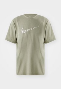 Oliwkowa bawełniana koszulka z okrągłym dekoltem i krótkimi rękawami. Na przedniej części znajduje się duże, teksturowane białe logo Nike w kształcie swooshu.