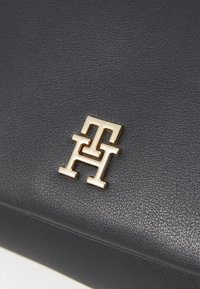 Mornarica kožna torba s sjajnim zlatnim logotipom. Glatka tekstura s kompaktnim pravokutnim oblikom i minimalnim detaljima šivanja.